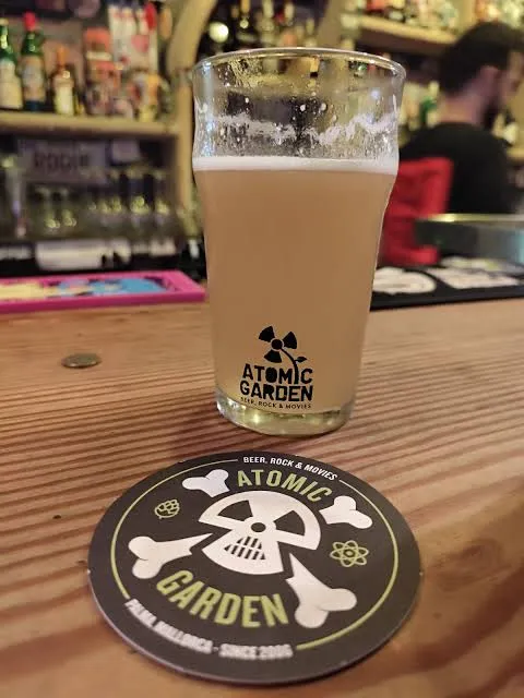 Vaso de cerveza con la marca de Atomic Garden junto a un posavasos sobre la mesa de madera del local