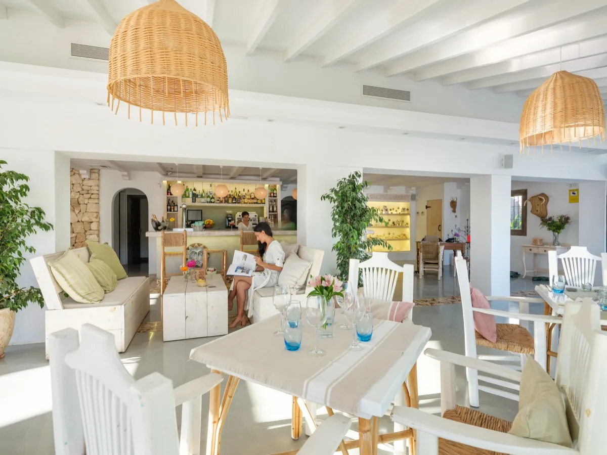 Zona de lounge y bar de Cabau Hotels, luminosa y en tonos claros, con una clienta leyendo junto a la barra