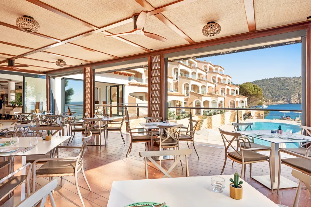 Terraza-restaurante de Cabau Hotels con vistas a la piscina, el edificio del hotel y la cala al fondo