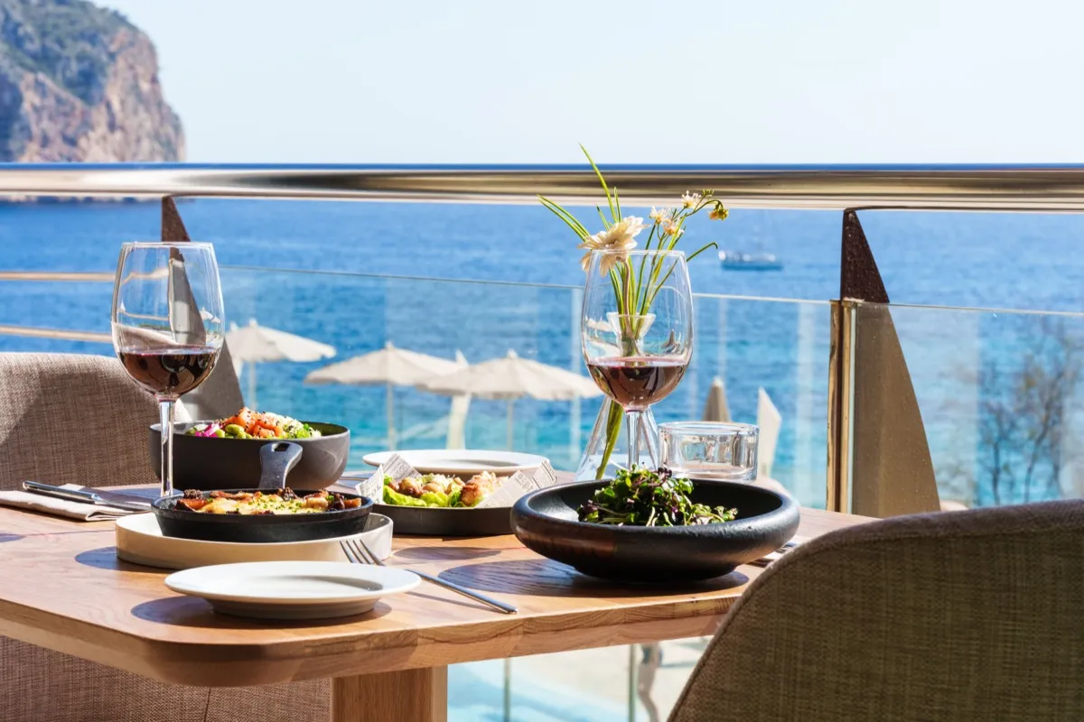 Mesa preparada en una terraza de Cabau Hotels con vistas al mar, copas de vino y la cala al fondo