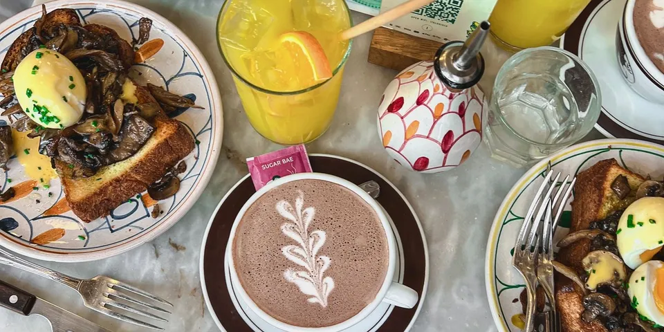 Mesa de cafetería con un brunch de fin de semana: tostadas, huevos, café y zumo, vista cenital