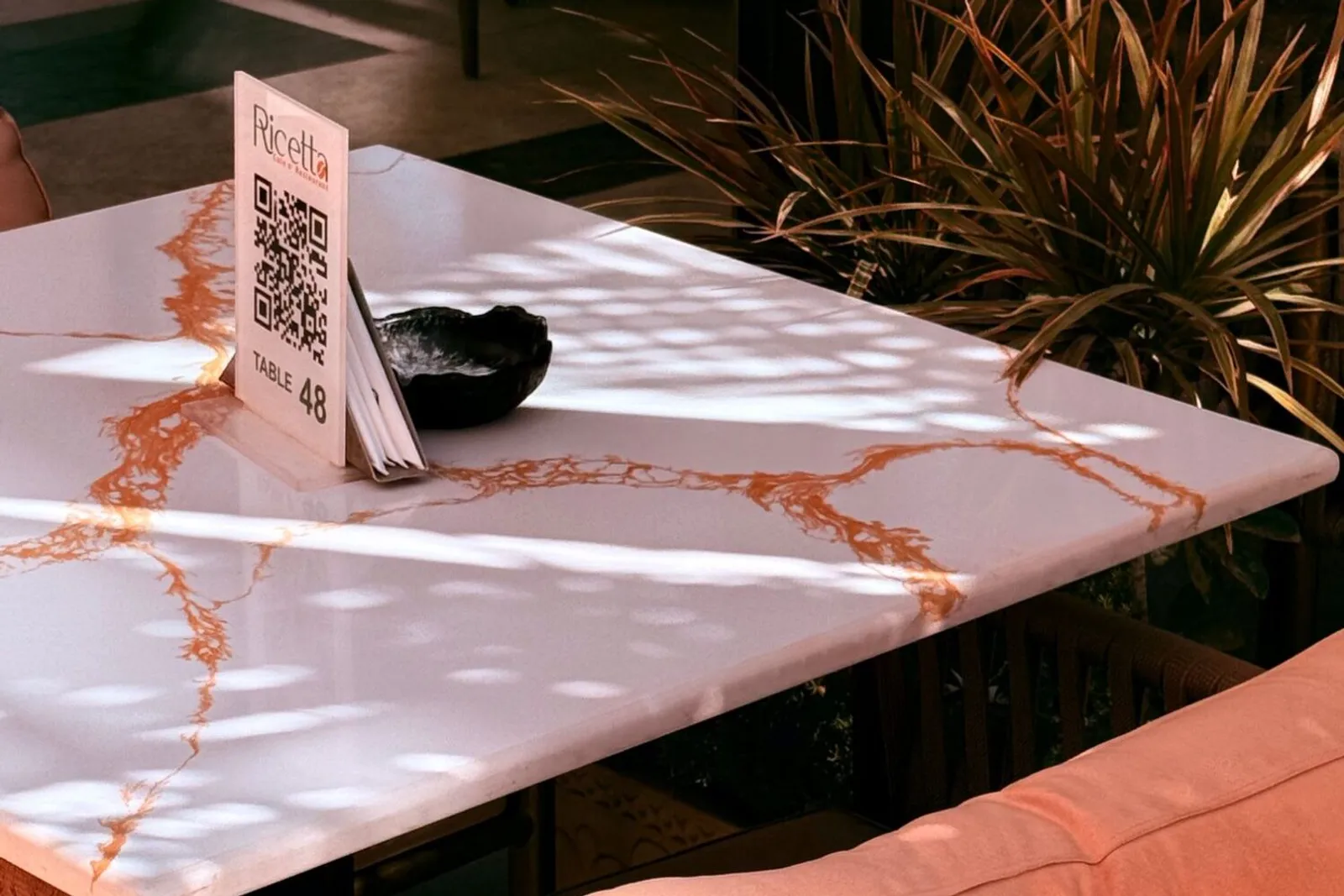 Soporte de mesa con un código QR sobre una mesa de mármol en la terraza de un restaurante, con luz de tarde