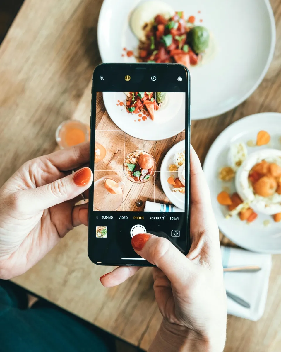 Mano sosteniendo un móvil fotografiando un plato sobre una mesa de bar con luz natural lateral